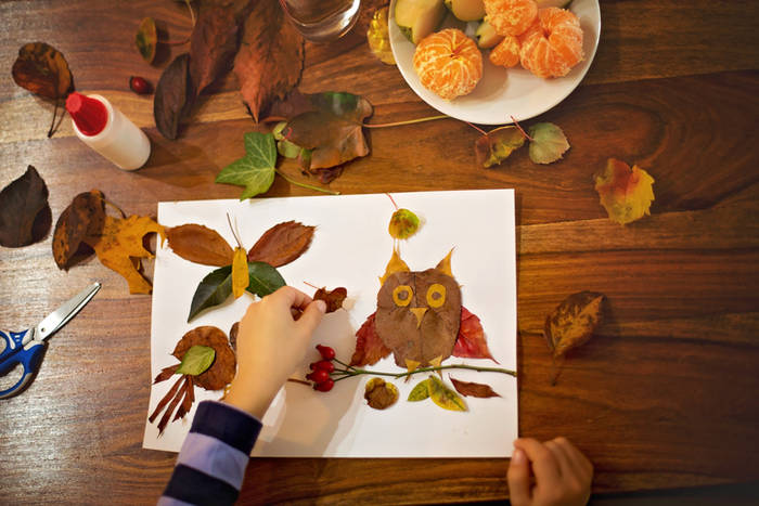 Sweet child, boy, applying leaves using glue while doing arts and crafts in school, autumntime